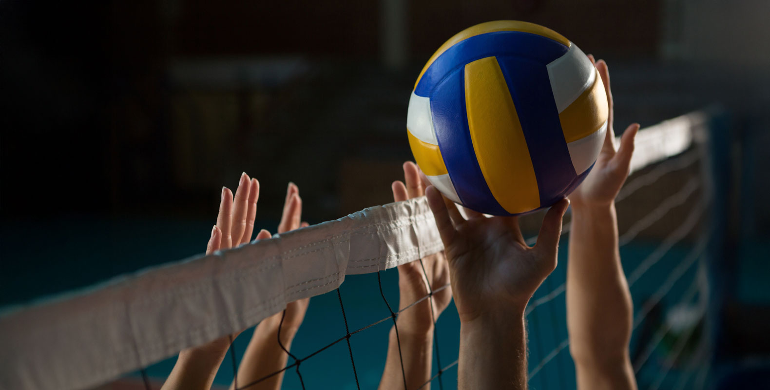 A volleyball in mid-air as multiple hands reach for it over the net during a game.