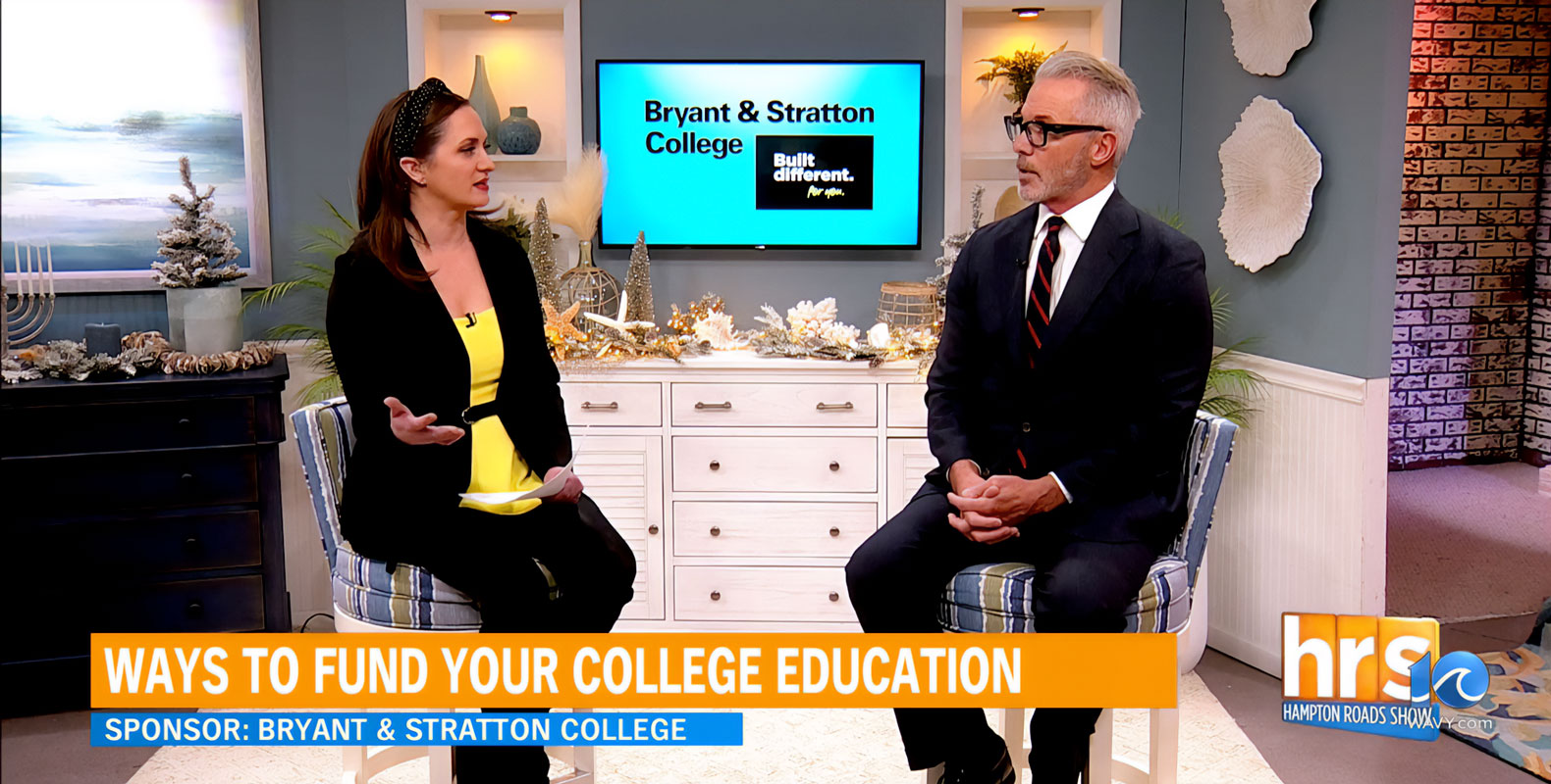 Two people sitting in a studio discussing ways to fund college education, with a Bryant & Stratton College sign in the background.