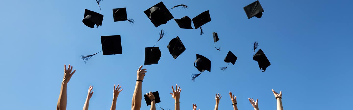 Graduation caps being tossed in the air against a clear blue sky, with several hands reaching upward in celebration.