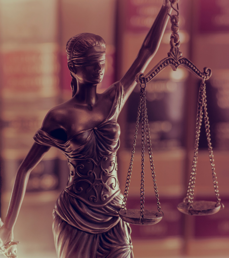 A bronze statue of Lady Justice holding balanced scales, wearing a blindfold, stands before blurred legal books—symbolizing fairness and impartiality in law, values upheld by every dedicated Sheriff and Deputy Sheriff.
