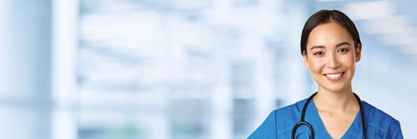 A smiling healthcare professional in blue scrubs and a stethoscope stands against a blurred background, suggesting a hospital setting—perfect for promoting a Nursing Faculty job fair.