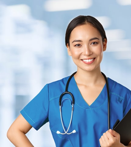A smiling nurse wearing blue scrubs and a stethoscope stands indoors, holding a black folder at a job fair, with a blurred hospital background.
