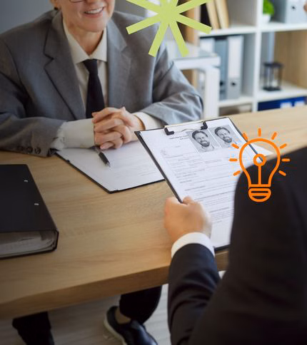 Two people in business attire sit across a desk during a job interview; one holds a clipboard with resumes, while the other smiles with hands folded. Decorative illustrations of a star and lightbulb overlay the image, highlighting professional development.