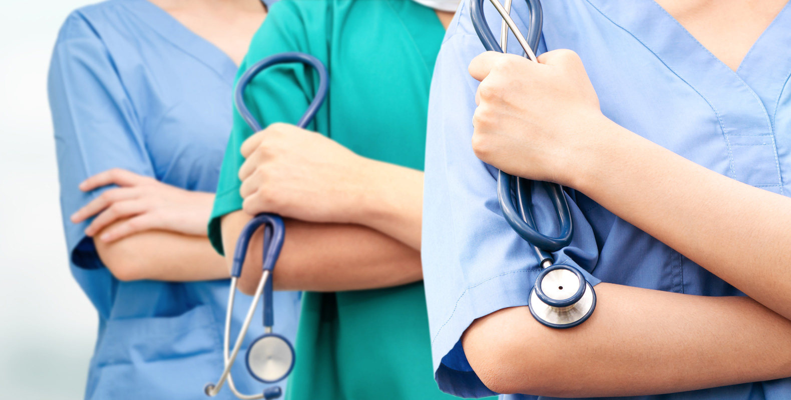 Three healthcare professionals stand side by side in scrubs, each holding a stethoscope. Their faces are out of frame, focusing on their uniforms and crossed arms, representing teamwork in a medical setting.