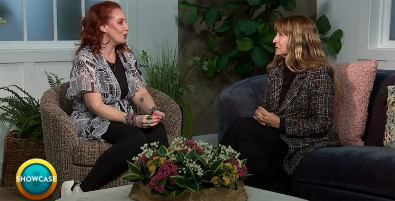 Two women sit facing each other in a cozy, well-lit living room, chatting about the upcoming Spring Semester at Bryant & Stratton College. A round table with a floral arrangement separates them, and a “SHOWCASE” logo appears in the bottom left corner.